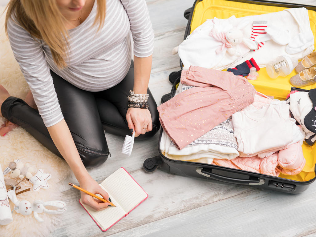 Pregnant woman sitting next to an open suitcase filled with baby clothes