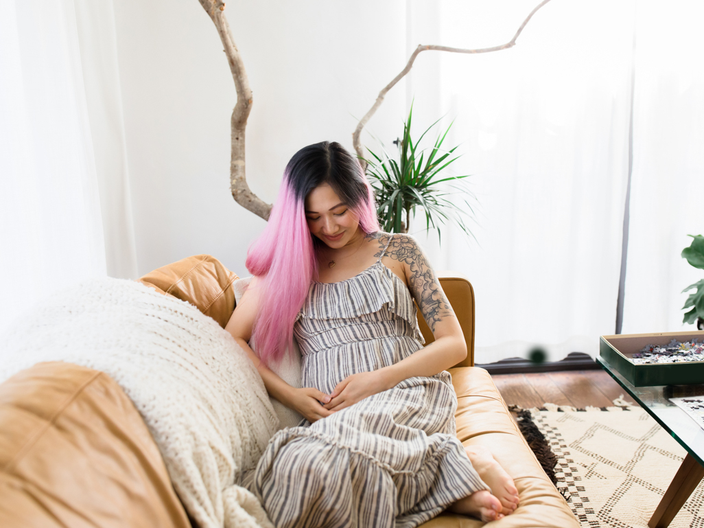 Pregnant woman sitting down on the sofa with her hands on her bump