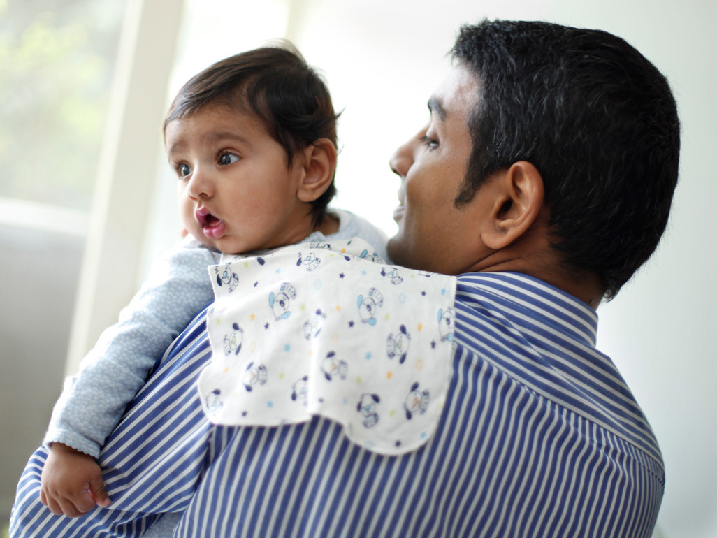 father holding a baby firmly against his shoulder and trying to make him/her burp