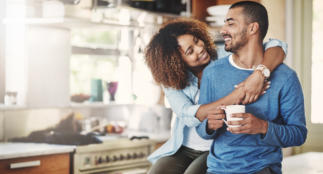 woman hugging mans neck while sitting in kitchen