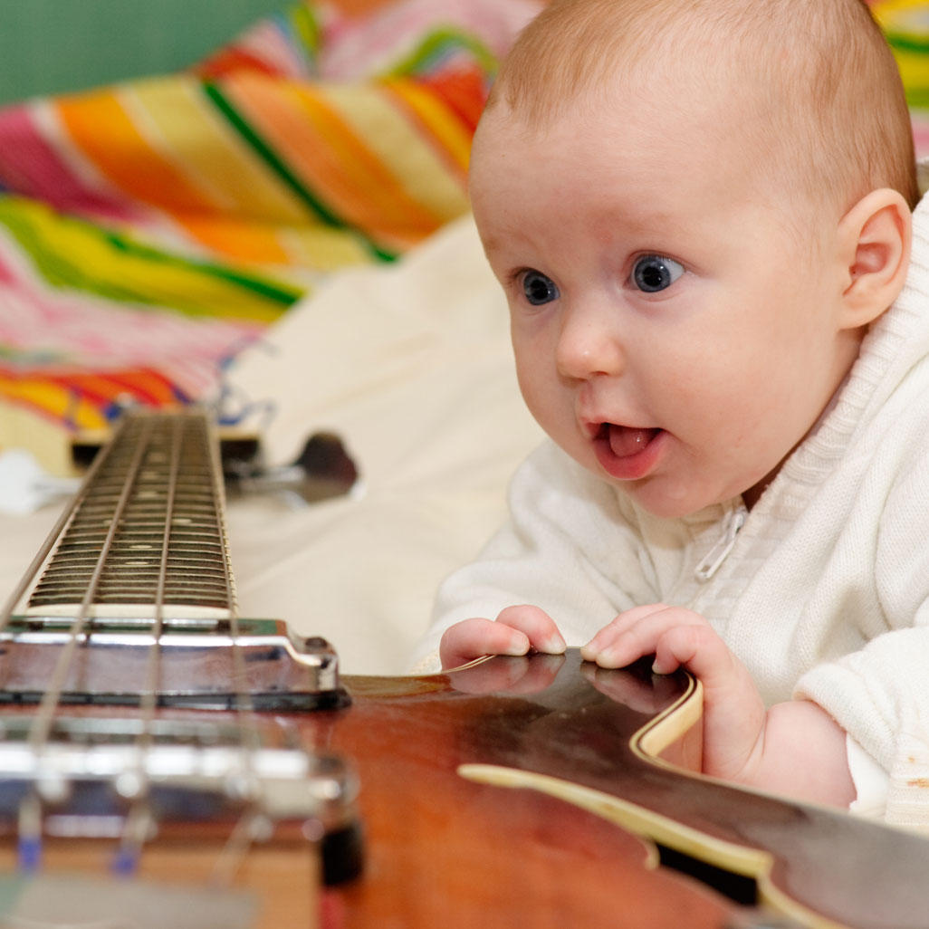 baby eyeing a guitar with curious look on face