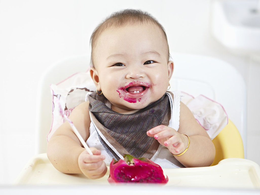 baby eating in a high chair with food all over her face