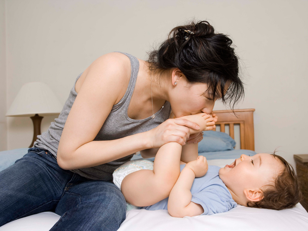 woman kissing baby's feet while baby is laying on the bed