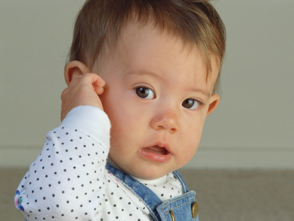 baby holding ear and looking at camera