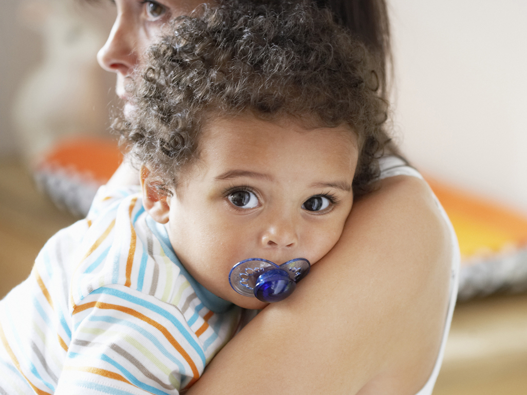 child with pacifier in his mouth, embraced by his parent