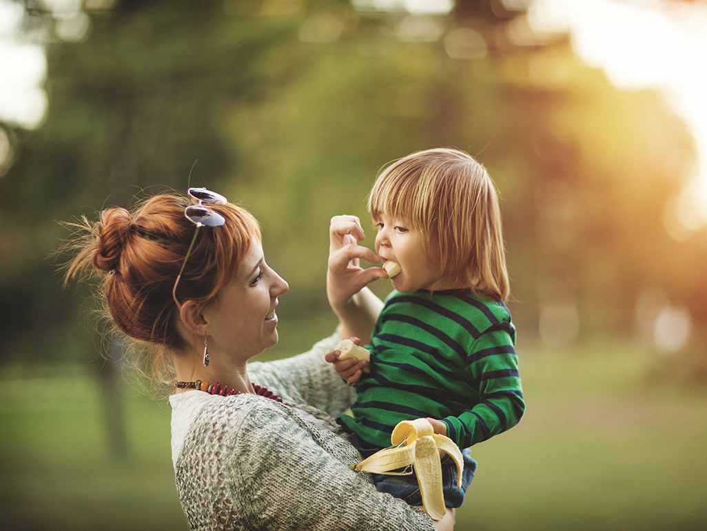 mother feeding her child outdoor with a banana