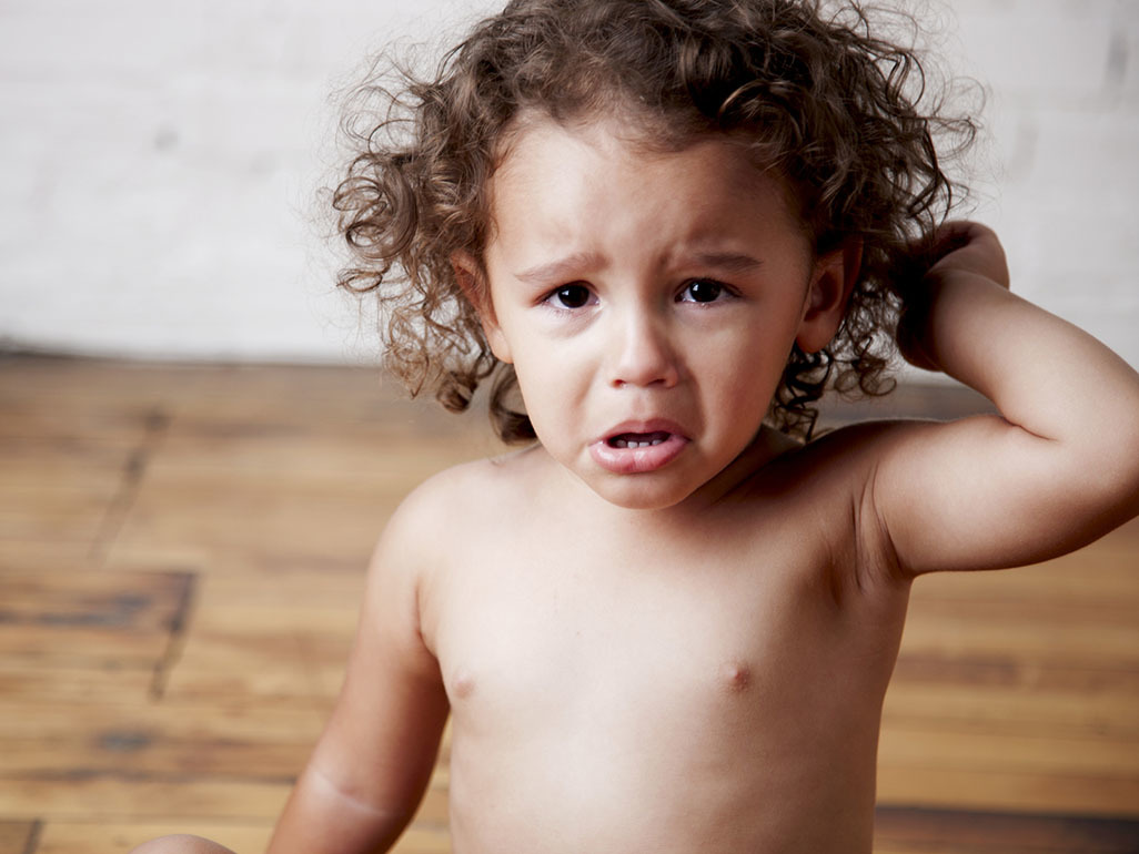 A toddler looking upset, with his hand on his head.