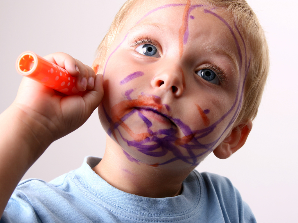 toddler with painted symbols on its face holding a crayon in the hand