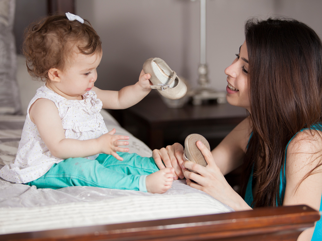 baby holding a shoe and mother making her wear one