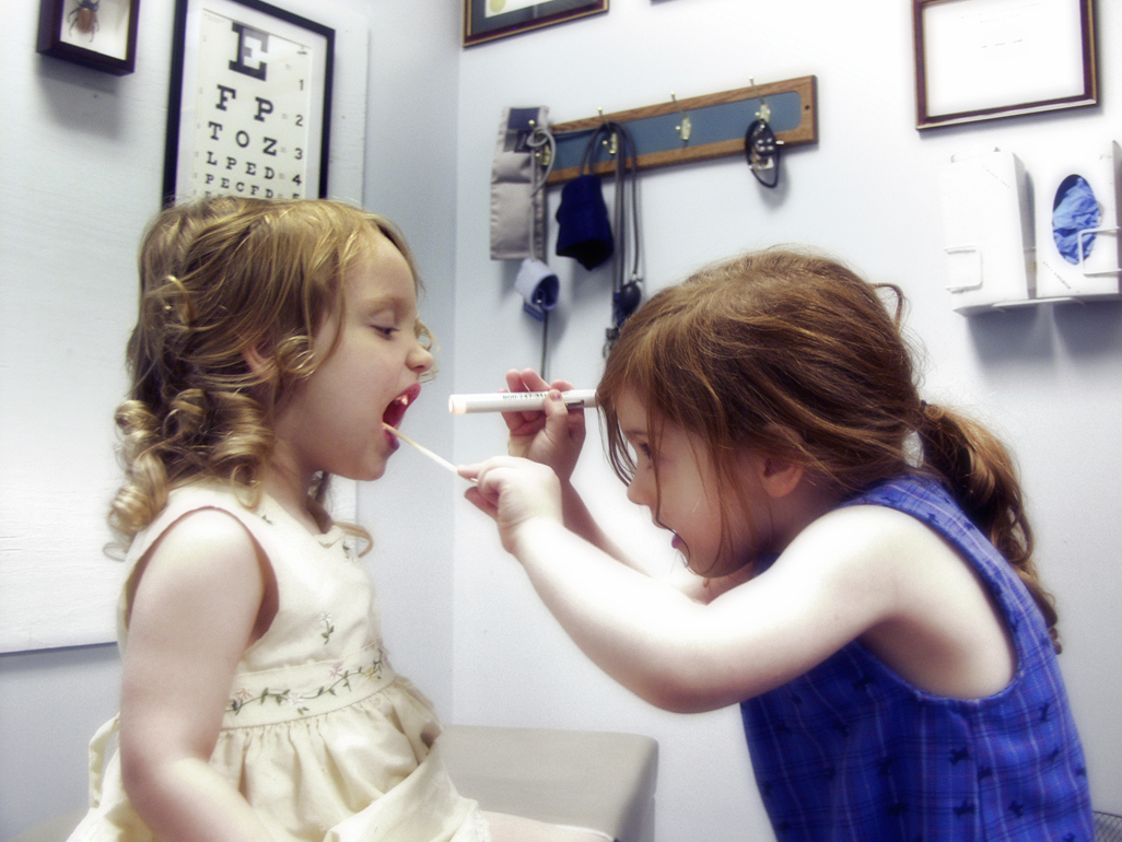 two little girls playing doctor, one is examining the other's throat