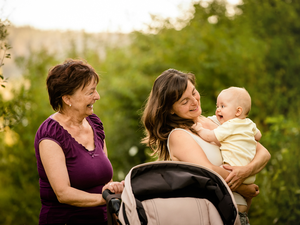 Two people on a walk with a baby, one pushing a stroller and one holding the baby