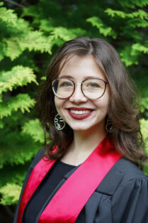 Full color portrait photo of Bailey DeSimone at her college graduation in a graduate robe with a sash.