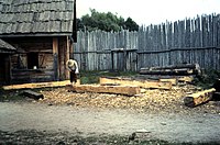 A craftsman uses an adze to square beams, and to recreate 17th-century colonial life.