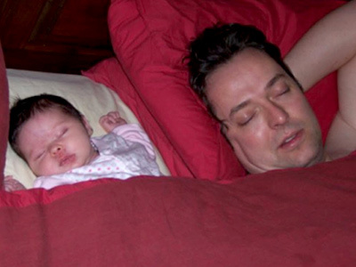 Dad and baby daughter sleeping in bed sharing a blanket