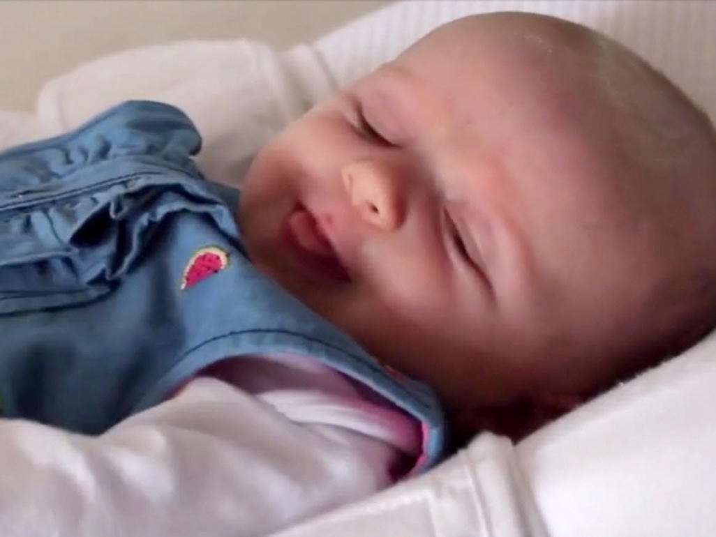 Baby wearing a blue dress lying on her back sticking tongue out