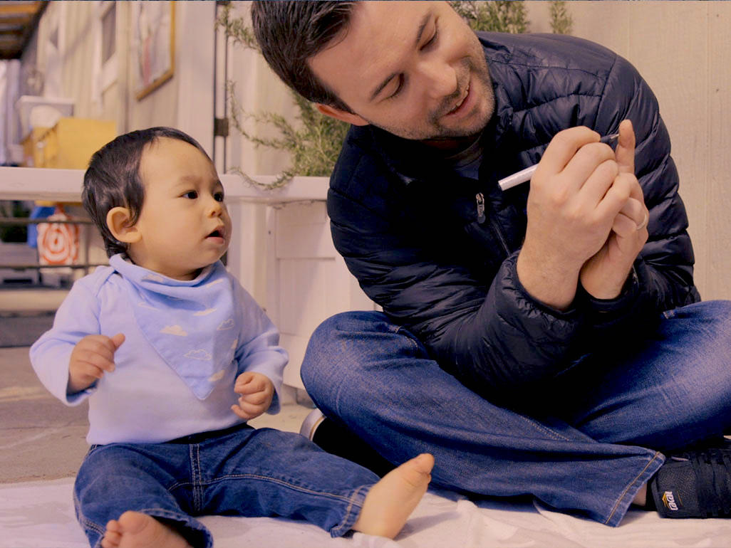 Dad and sitting toddler looking at a pen