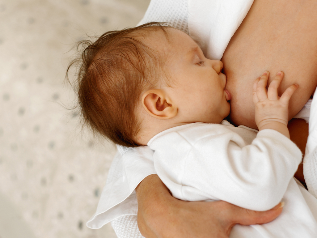 Close up of baby dressed in white breastfeeding with eyes closed