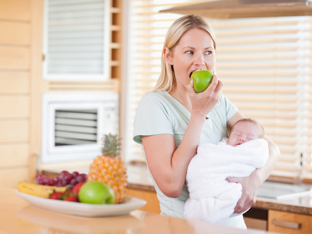 Mum holding baby while eating an apple