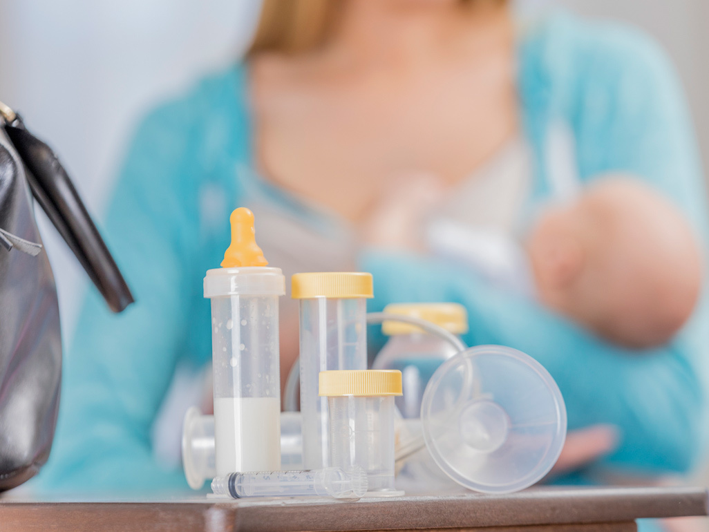 Breastmilk pump in foreground, mum holding her baby in background