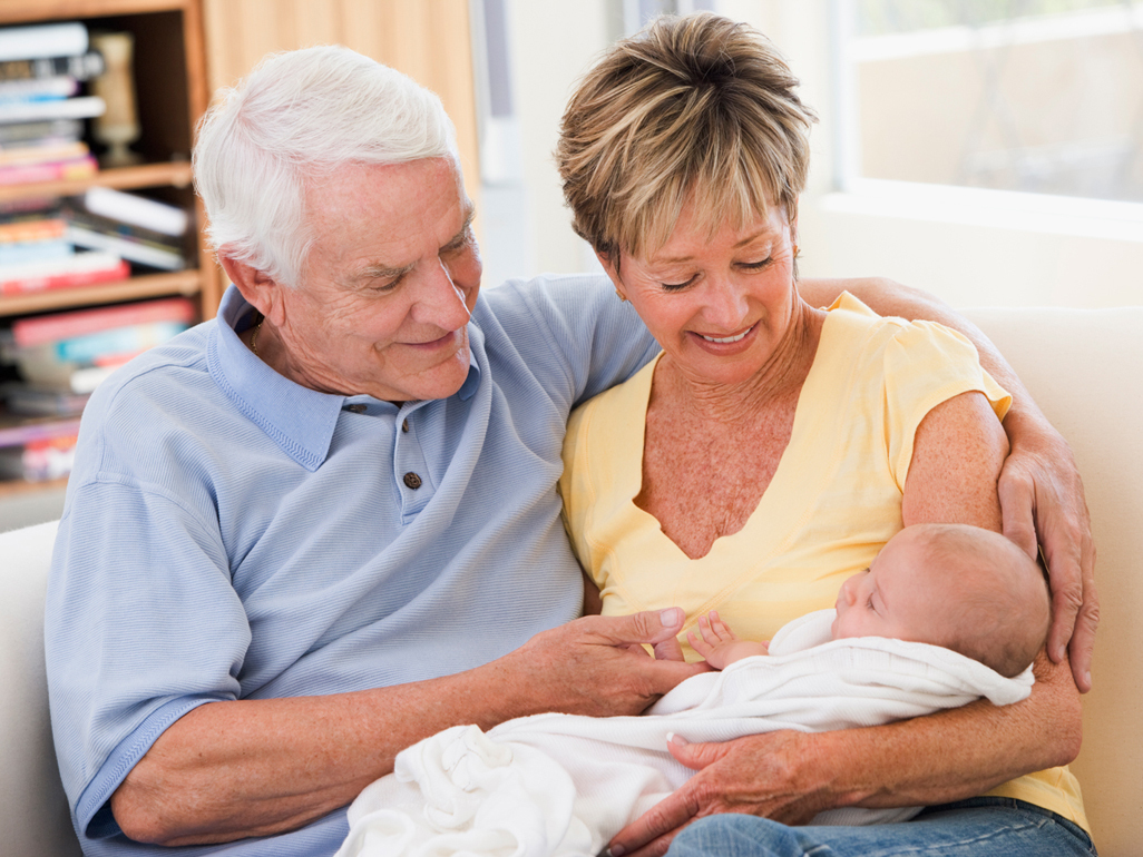 Grandparents sitting on a sofa and holding a newborn