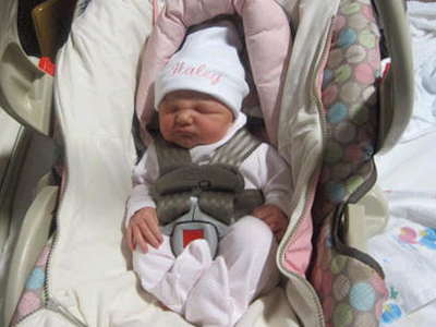 Newborn baby girl wearing a white romper and a white hat with the name "Haley" in pink letters