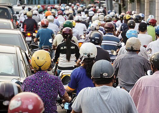 The roads of Ho Chi Minh City are packed with scooter traffic. One scooterist has a unique yellow helmet with a winky smile on the back of it, making him/her standout from others.