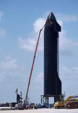 Photograph of a worker on an aerial work platform repairing a spacecraft's black heatshield