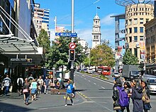 Pedestrians crossing a wide street which is flanked by storefronts