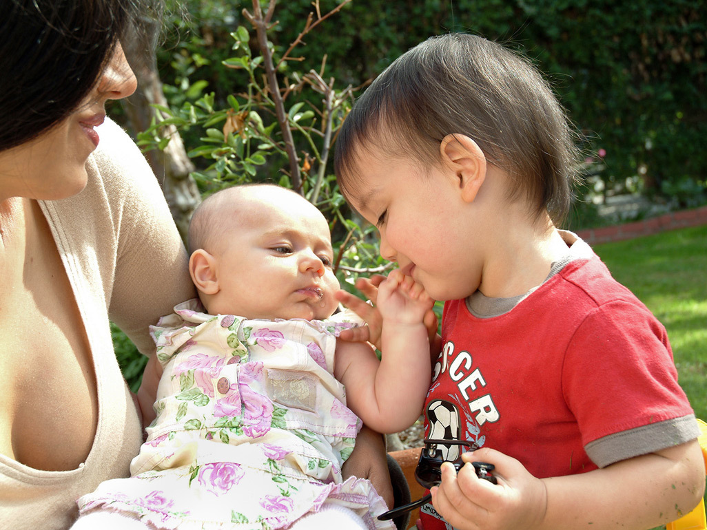 Baby in mum's arms gently touching toddler brother's face