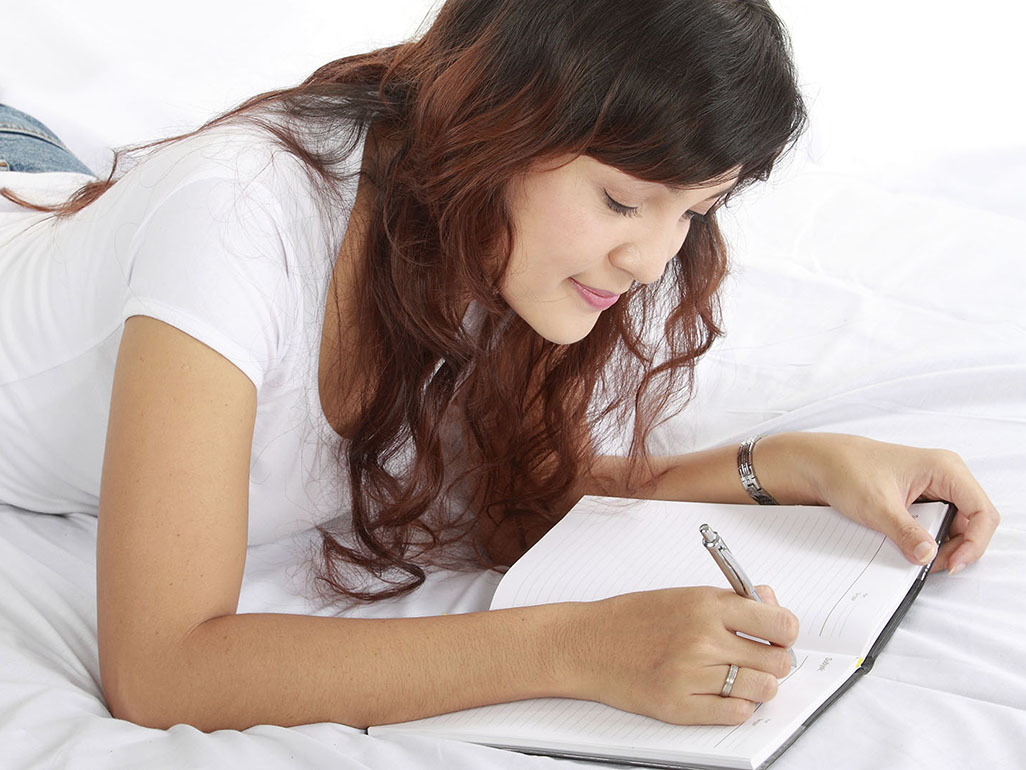 Pregnant woman lying on bed writing shopping list