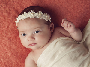 baby with lace headband lying on red cloth with body covered by sheet