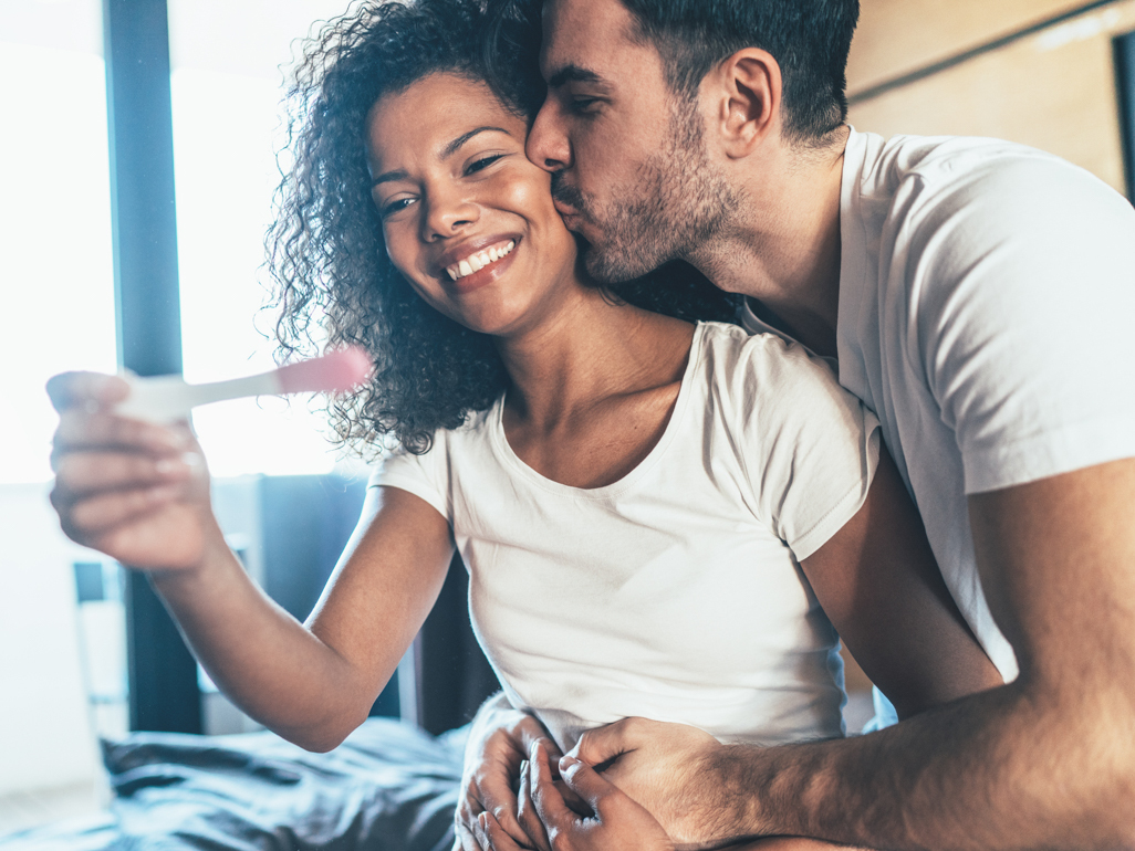 Woman holding up pregnancy test smiling with partner