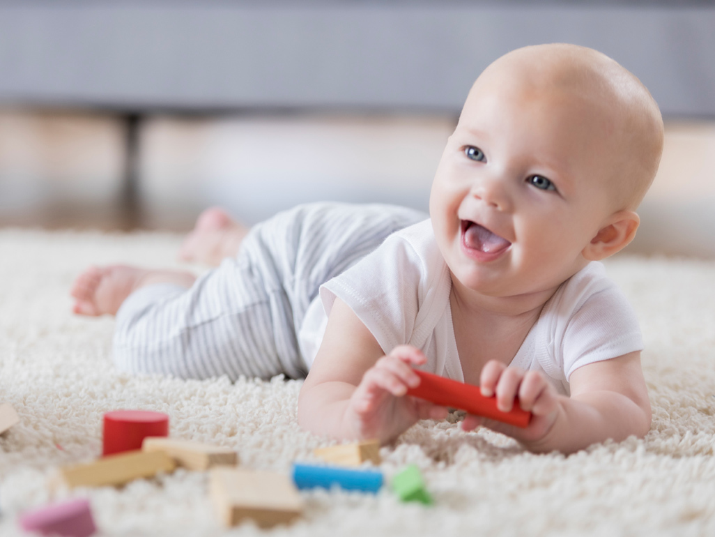 Baby playing and smiling on rug with toys