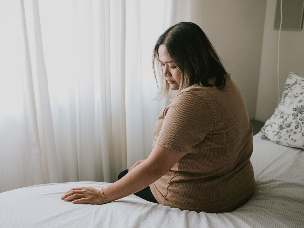 Mujer triste sentada en la cama de espaldas a la cámara