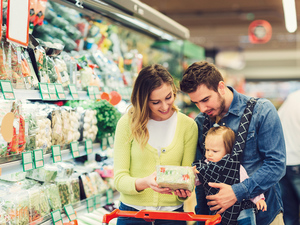 couple grocery shopping, while man is carrying baby girl in a baby carrier