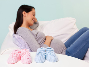 Pregnant mum sitting on a sofa with her hand on her bump with pink and blue booties in the foreground