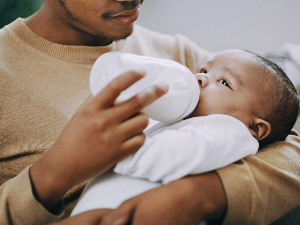 Homem negro amamenta bebê com mamadeira 