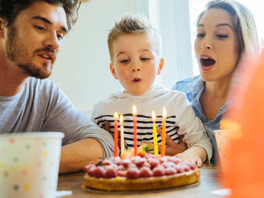 boy blowing out birthday candles with mother and father