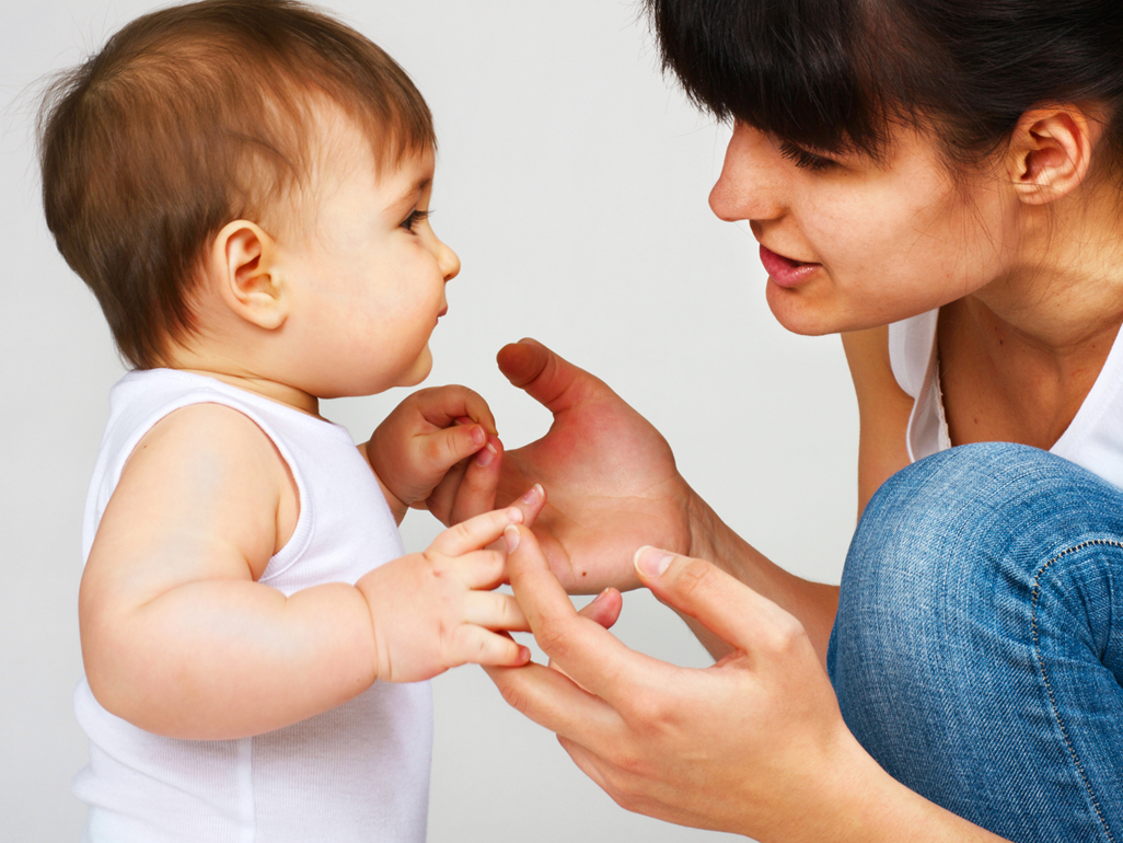 Mum kneeling by baby holding her hands and speaking to her