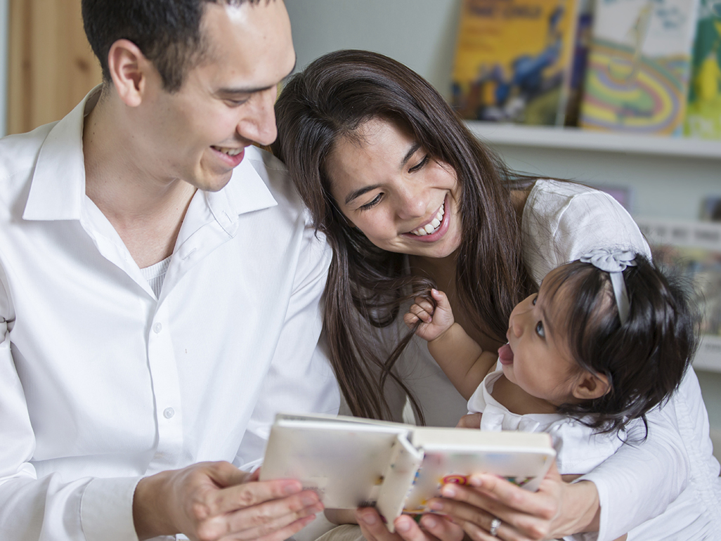 Parents showing a book to their daughter who's looking and speaking to them