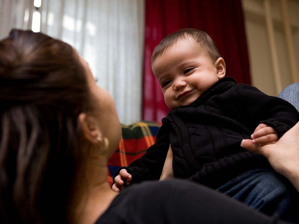 Mum lying on back holding smiling baby on her tummy