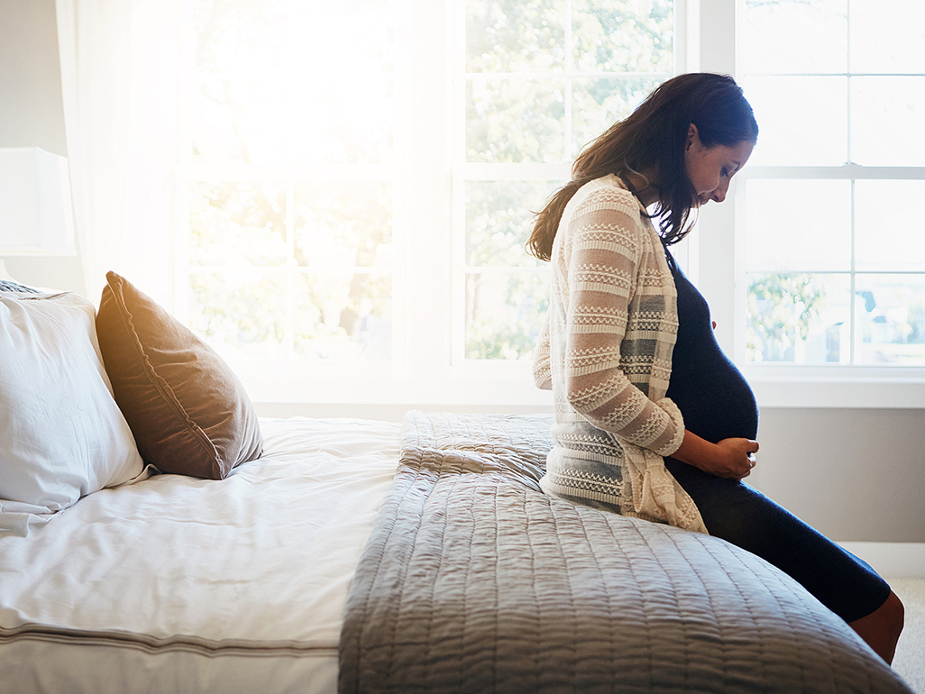 Pregnant woman sat on bed, hands on bump