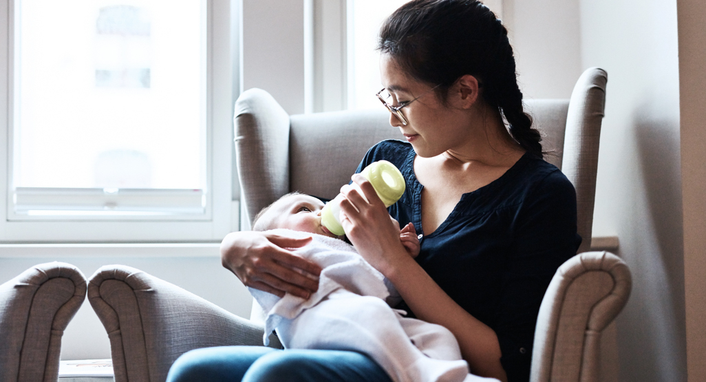 mother sitting in chair giving baby a bottle