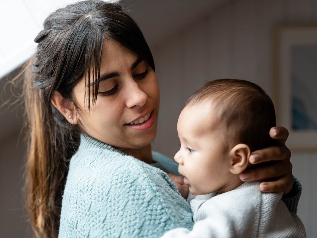 A mom holding and looking at her baby, text reads: BabyCenter Answers, Is it normal for babies to hiccup?