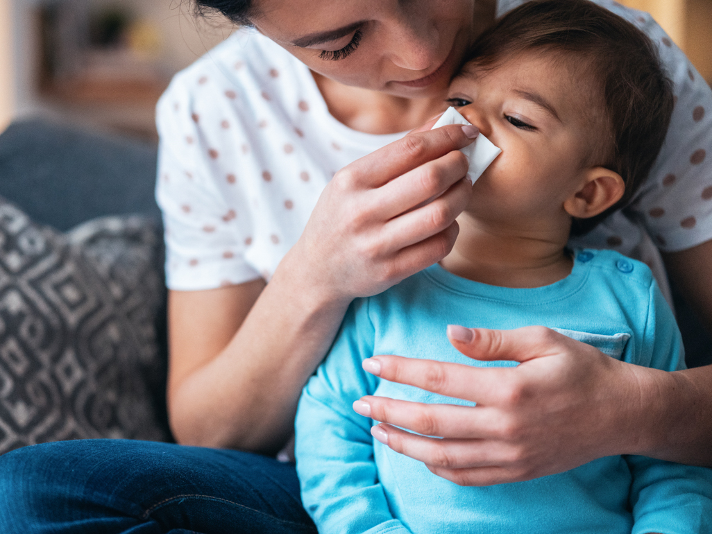 small boy getting help with blowing his nose