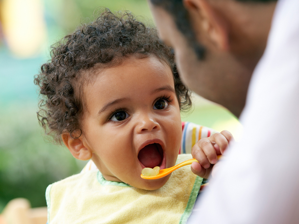 baby with curly hair and open mouth holding a spoon with some food