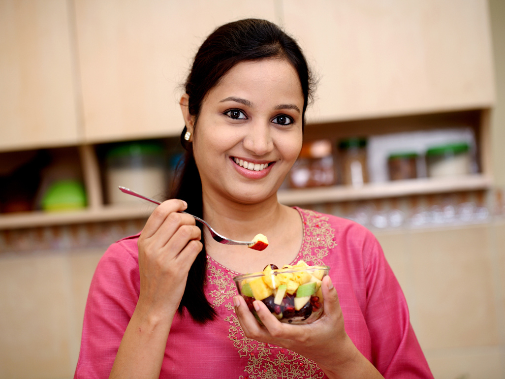 woman smiling and holding bowl of fruit in kitchen