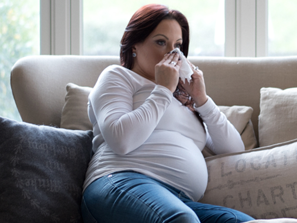 Pregnant woman with a cold blowing her nose