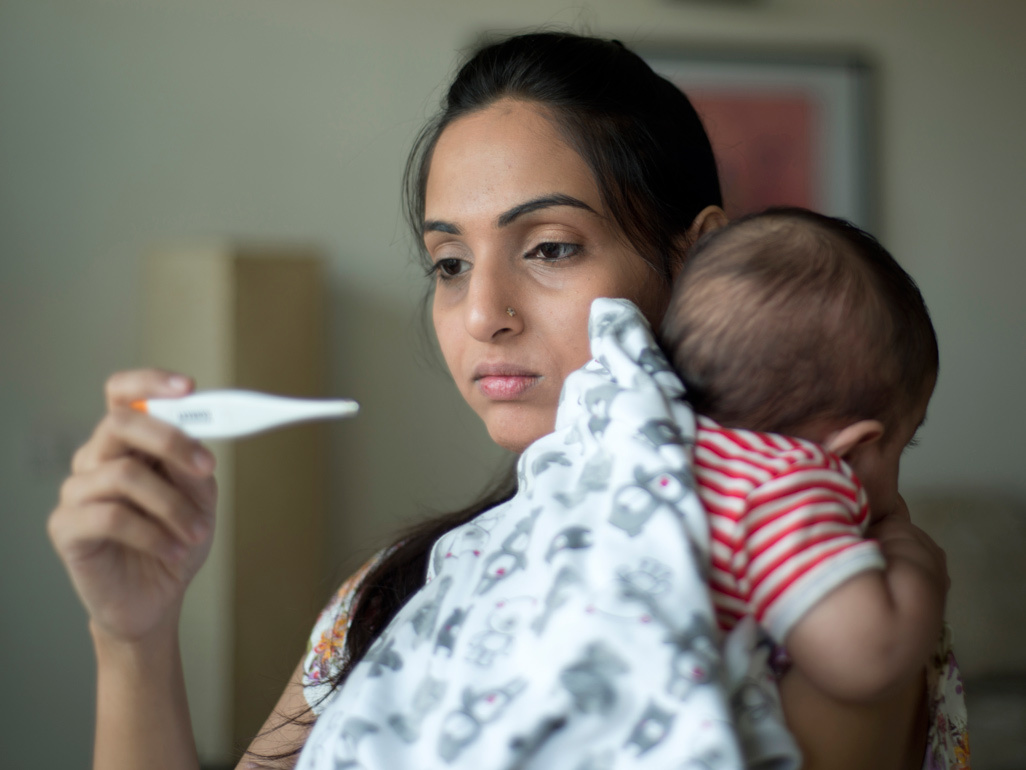 Mum checking thermometer while carrying her sick baby