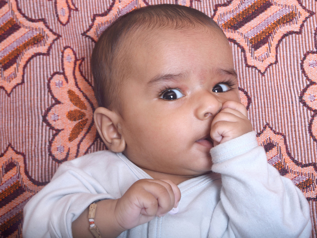 Baby with his hand in his mouth, looking into the camera